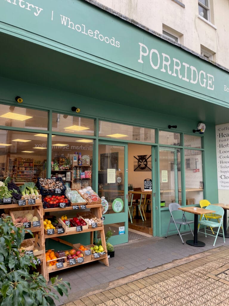 The PORRIDGE storefront at 13 Fore Street, Brixham, with sage-green fascia, pavement produce display, and cafe chairs out front